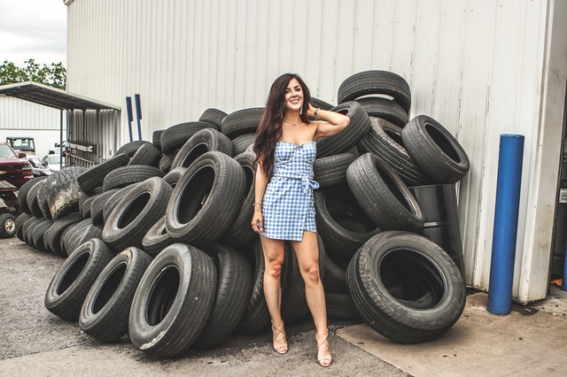 Žena v kockovaných šatách stojí pri kope pneumatík 